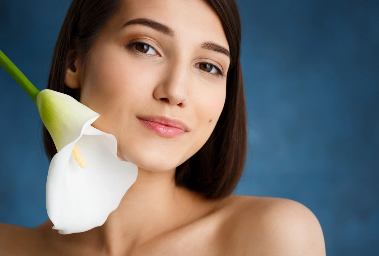 A woman with clear, radiant skin holding a white calla lily